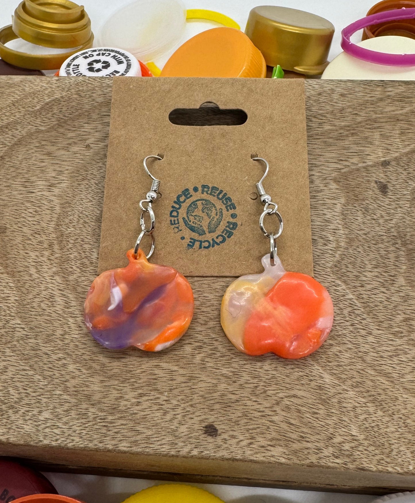 Pair of colorful earrings on a brown card with branding, surrounded by various items.