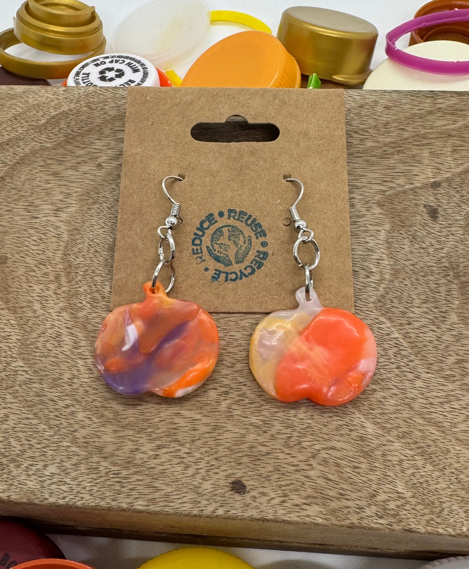 Pair of colorful earrings on a brown card with branding, surrounded by various items.