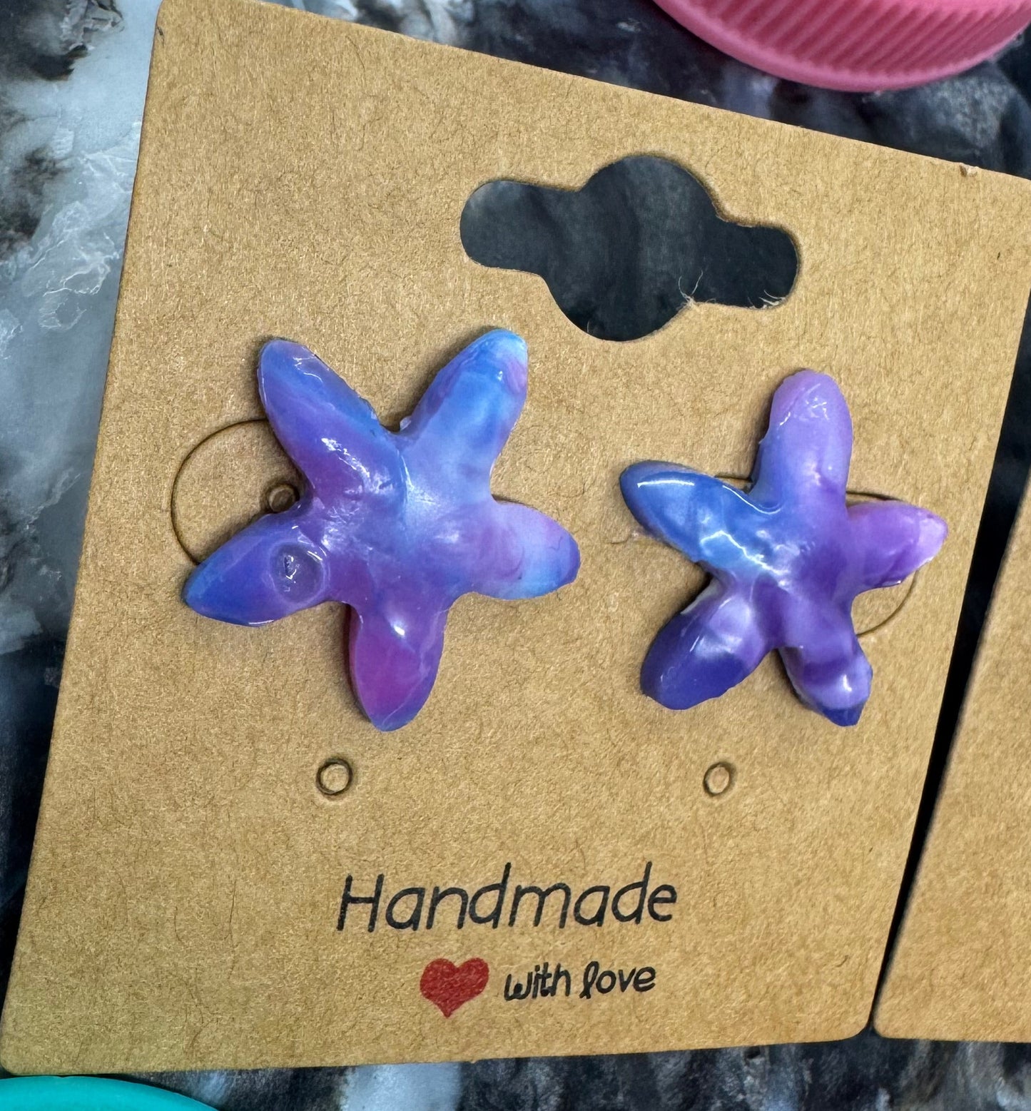 Purple starfish-shaped earrings on a cardboard display card with bottle caps in the background.