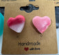 Heart-shaped pink earrings on a cardboard earring card with 'Handmade' text.