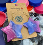 Star-shaped earrings on a cardboard backing with colorful bottle caps in the background