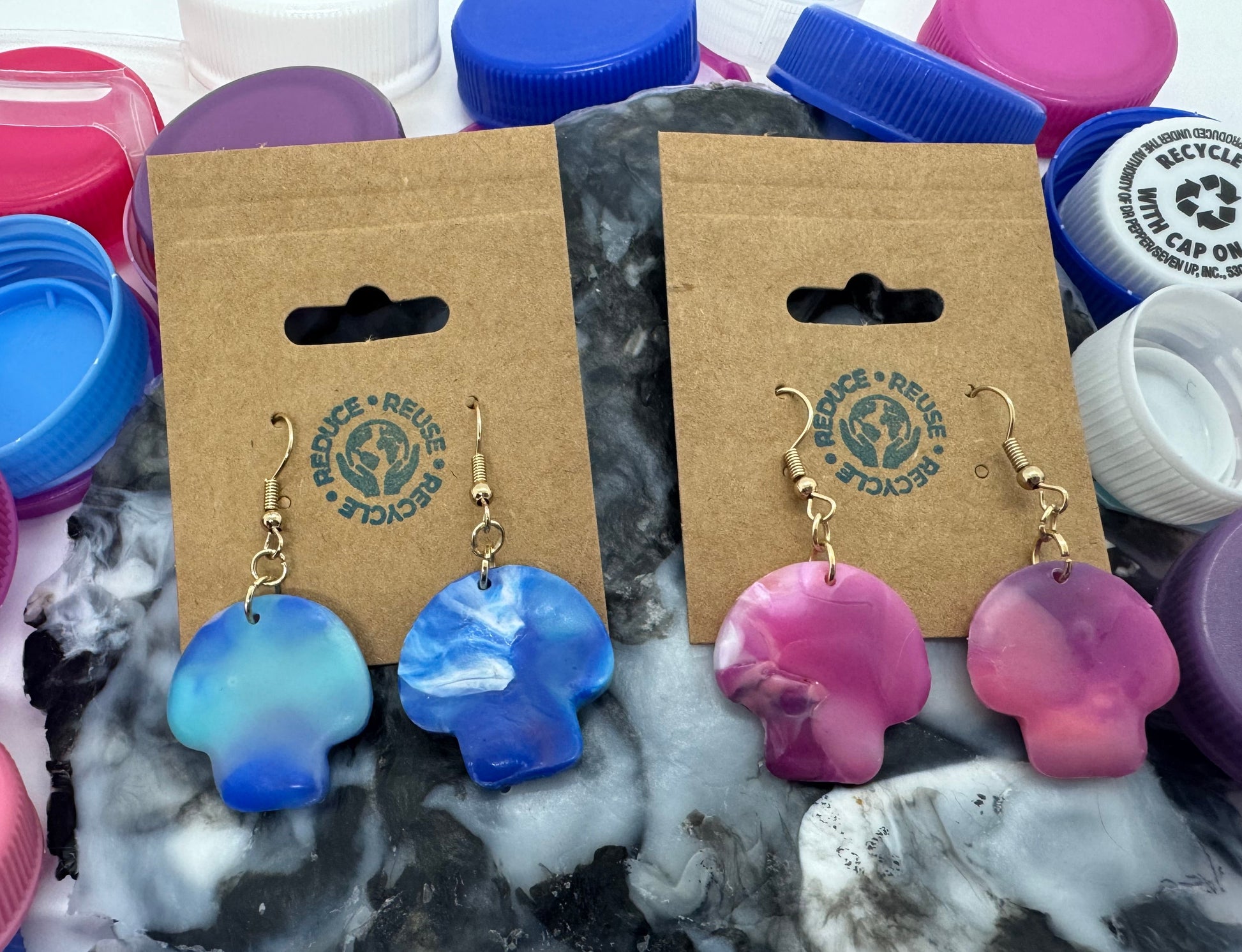 Pair of blue and pink earrings on display with colorful bottle caps in the background.