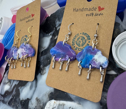 Pair of blue and purple earrings on a cardboard backing with 'Handmade' label, placed on a marble surface.