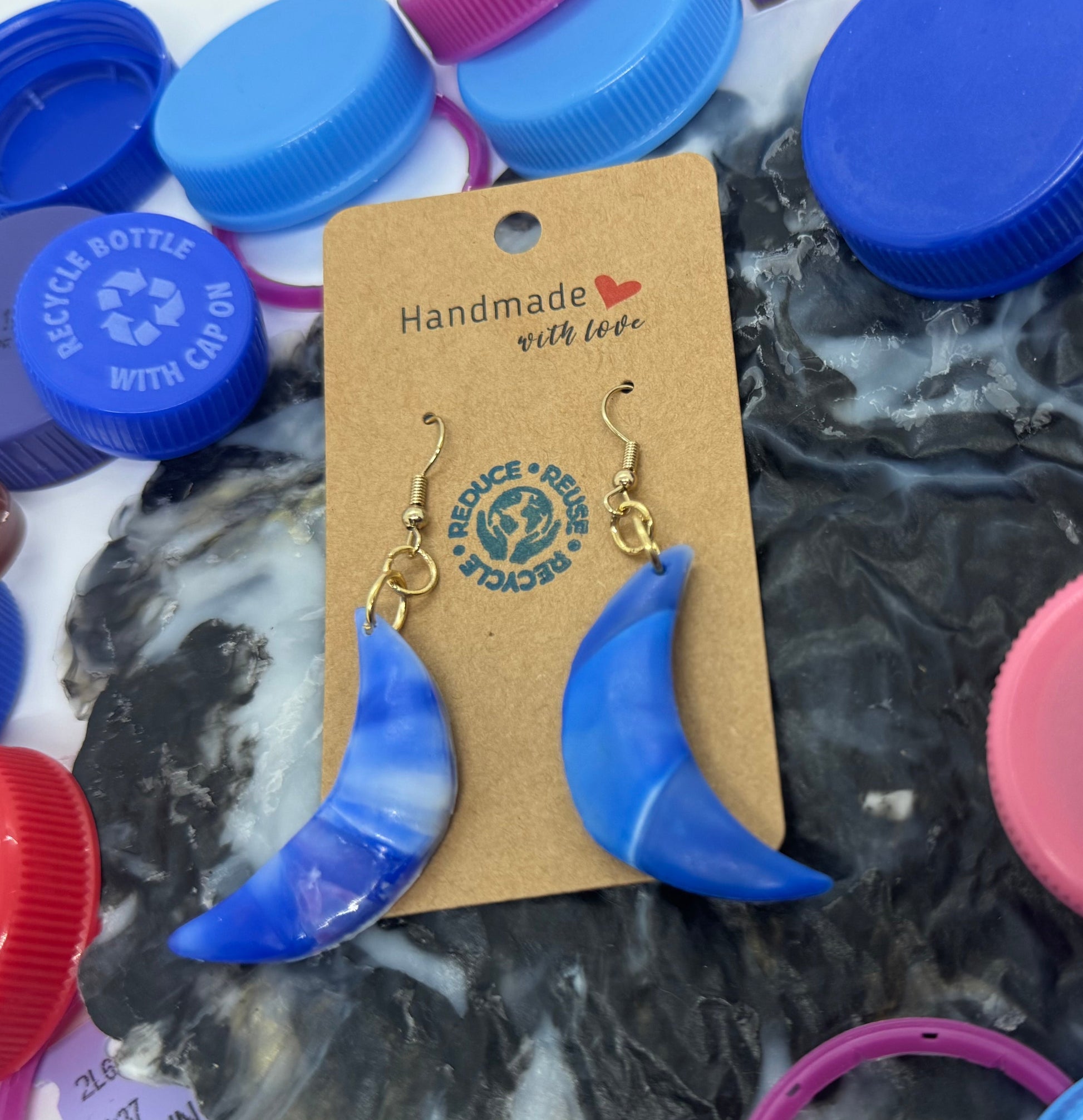 Blue crescent moon earrings on a card with colorful bottle caps in the background