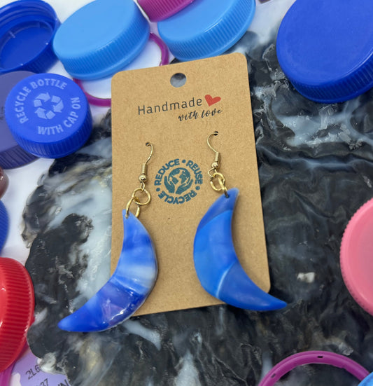 Blue crescent moon earrings on a card with colorful bottle caps in the background