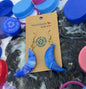 Blue crescent moon earrings on a card with colorful bottle caps in the background