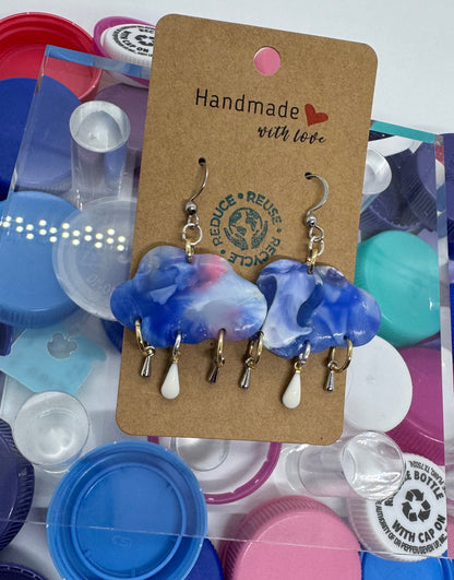 Pair of blue and white earrings on a 'Handmade' card with colorful bottle caps in the background.