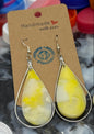 Two pairs of teardrop-shaped earrings on cards with colorful bottle caps in the background.