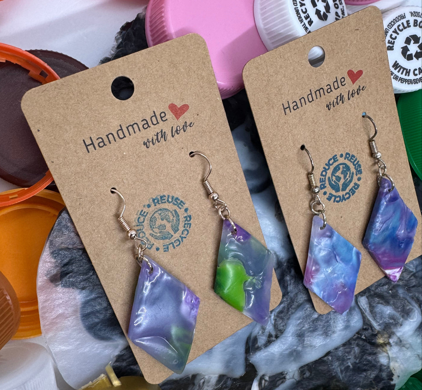 Handmade earrings on recycled plastic bottle cap tags with a colorful background of bottle caps.