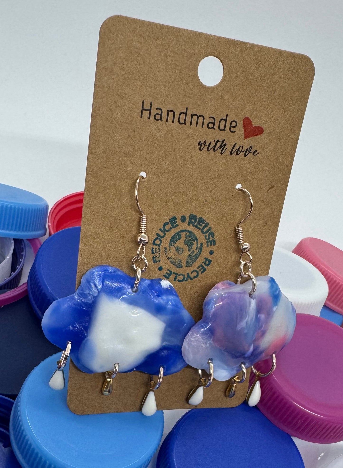 Pair of blue and white earrings on a 'Handmade with Love' card, surrounded by colorful bottle caps.