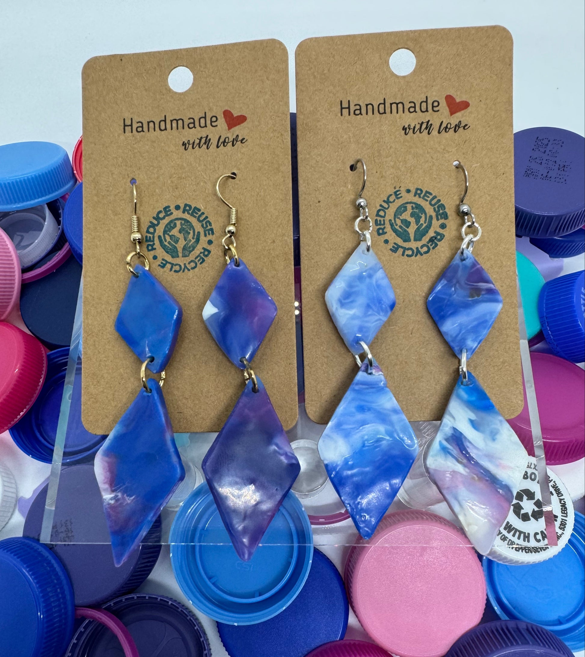 Pair of blue earrings on a cardboard card with colorful bottle caps in the background.