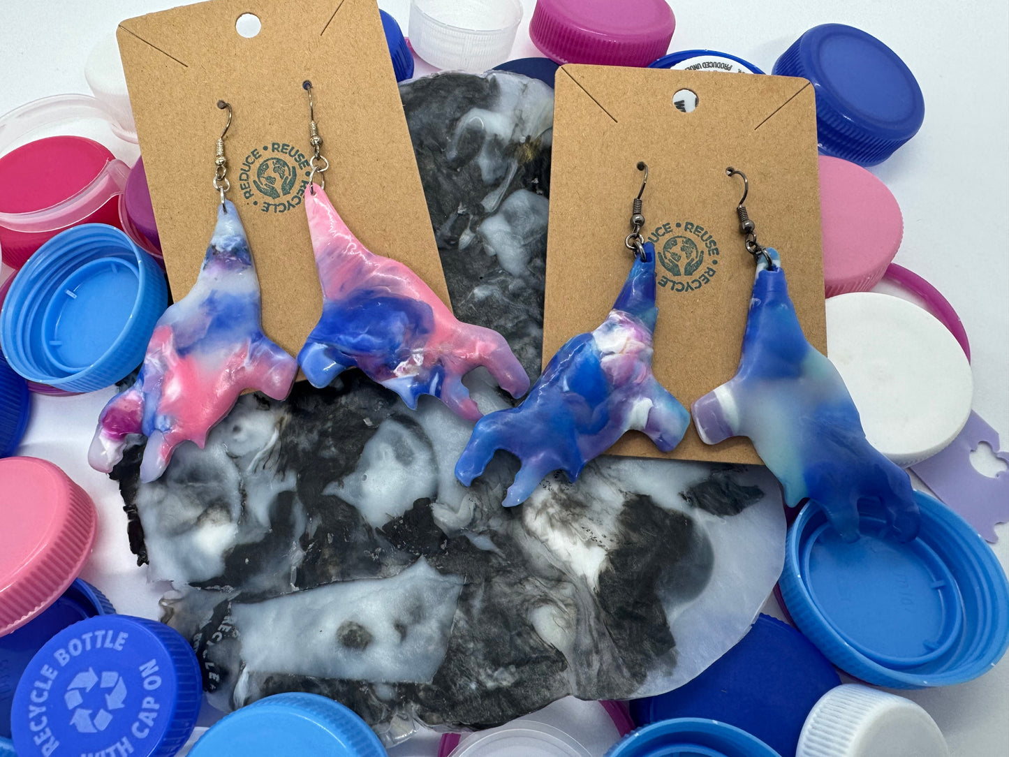 Colorful earrings on display with packaging and plastic bottle caps in the background