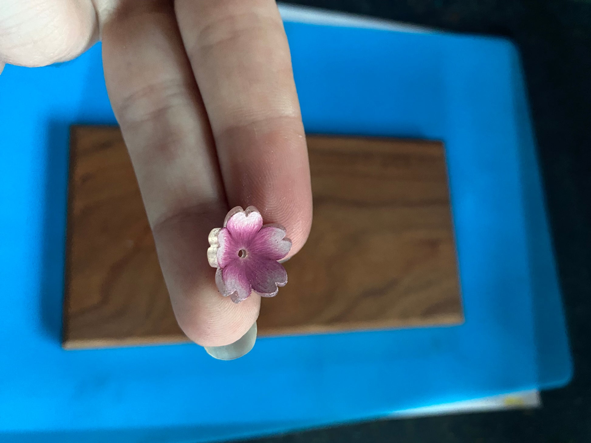 Hand holding a small pink flower-shaped object against a blue and wooden background