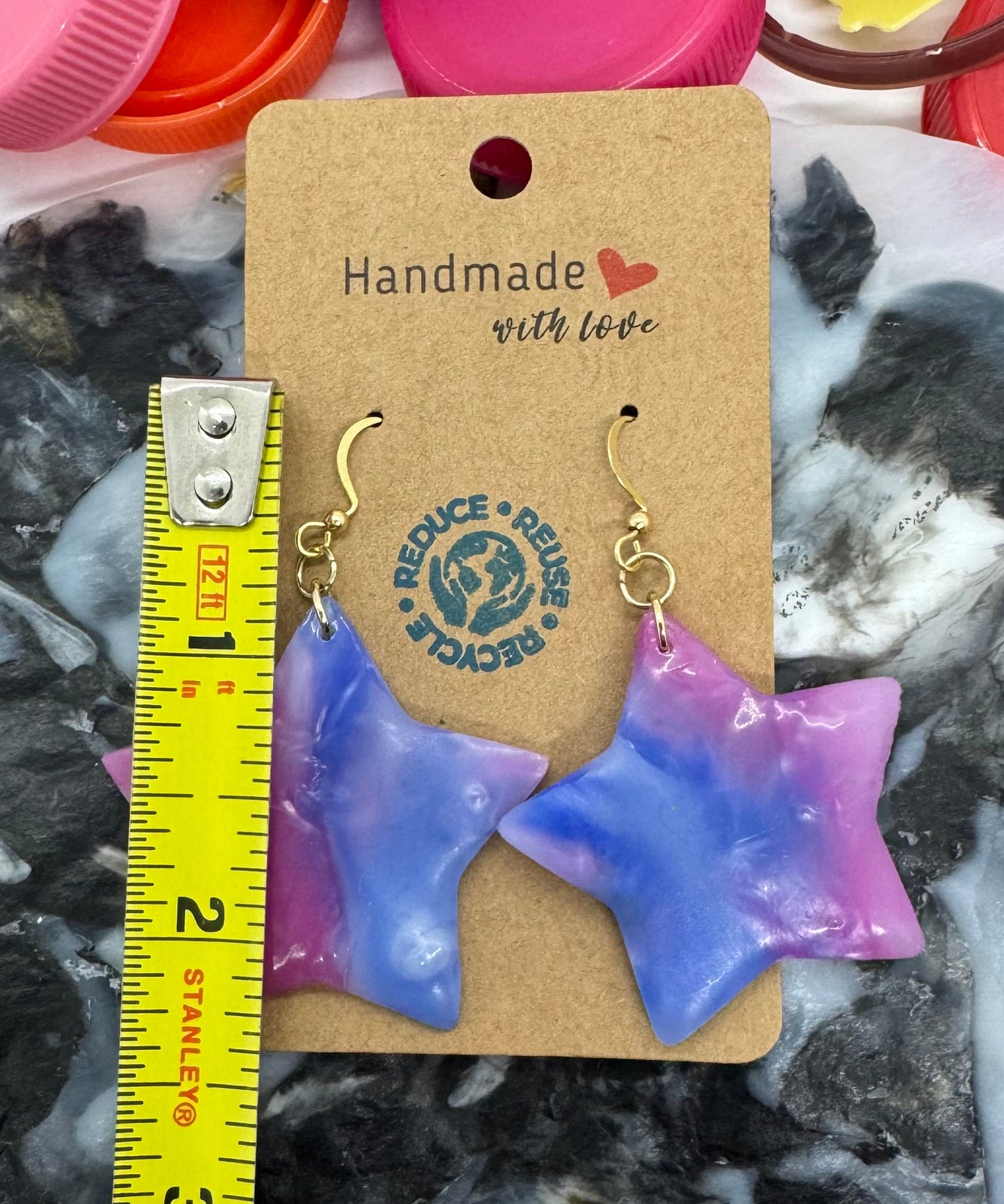Star-shaped earrings on a card with a measuring tape, surrounded by colorful bottle caps.