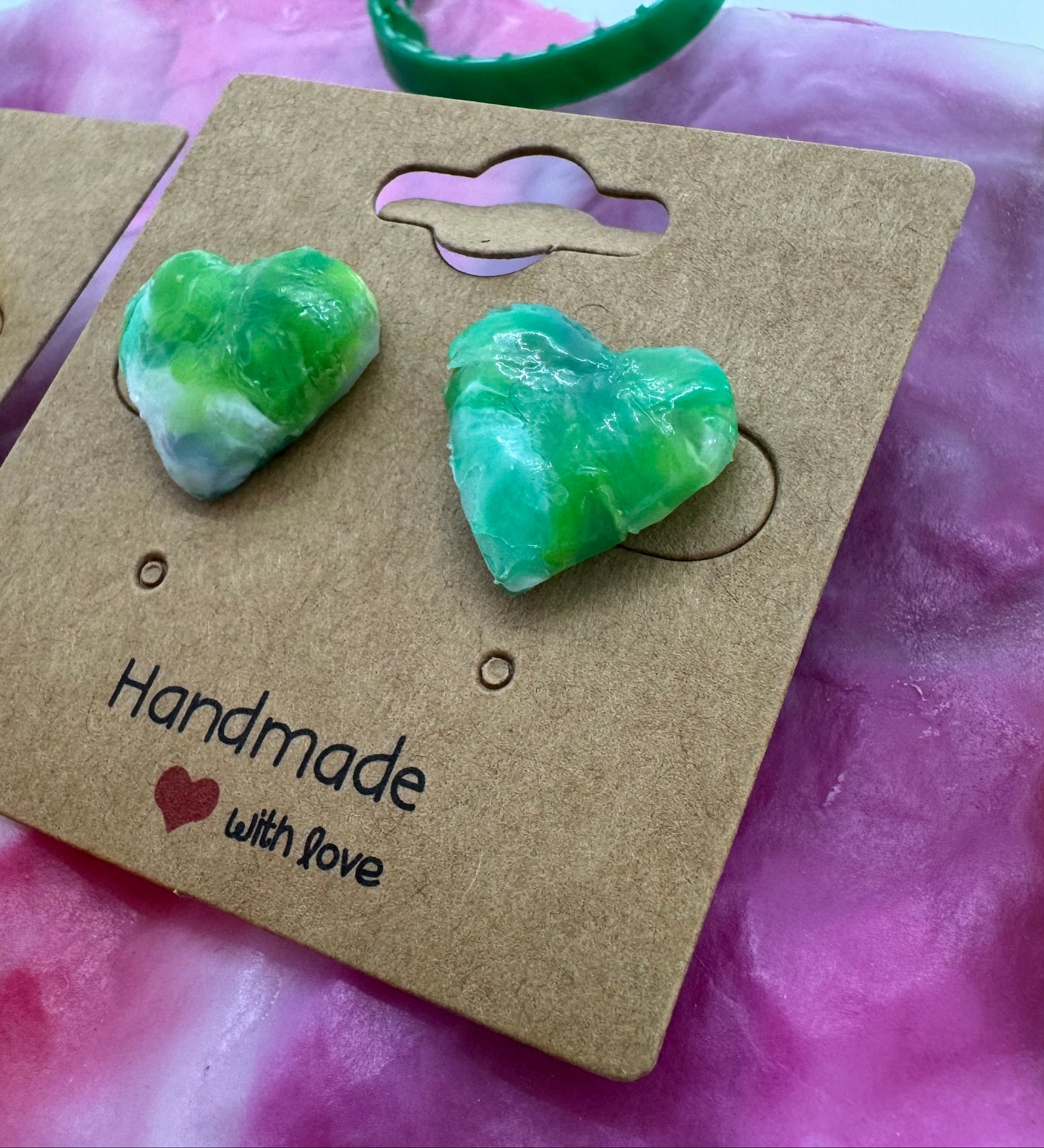 Green heart-shaped earrings on a brown card with 'Handmade with Love' text, against a colorful background.