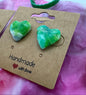 Green heart-shaped earrings on a brown card with 'Handmade with Love' text, against a colorful background.