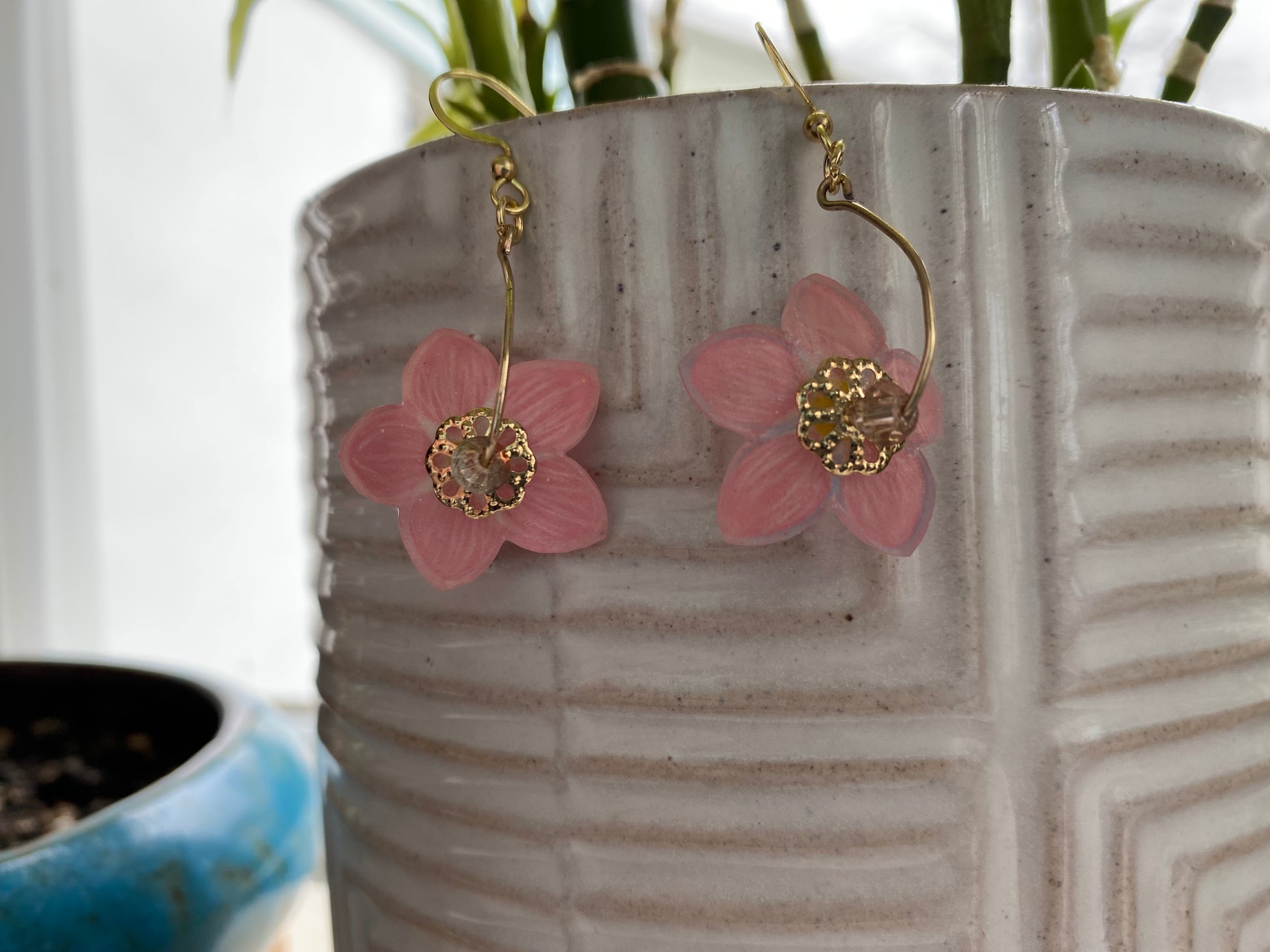 Pink flower earrings with gold centers on a textured white surface.