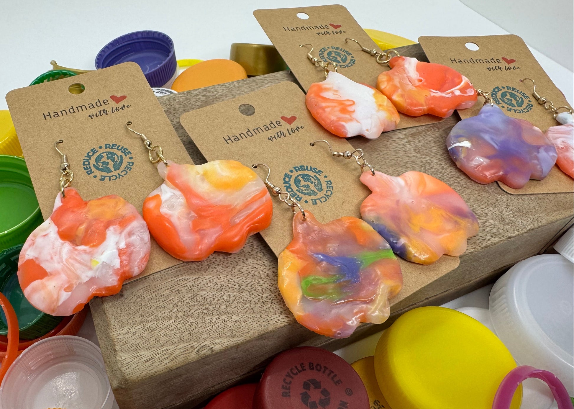 Colorful recycled plastic earrings on display with packaging and bottle caps in the background.