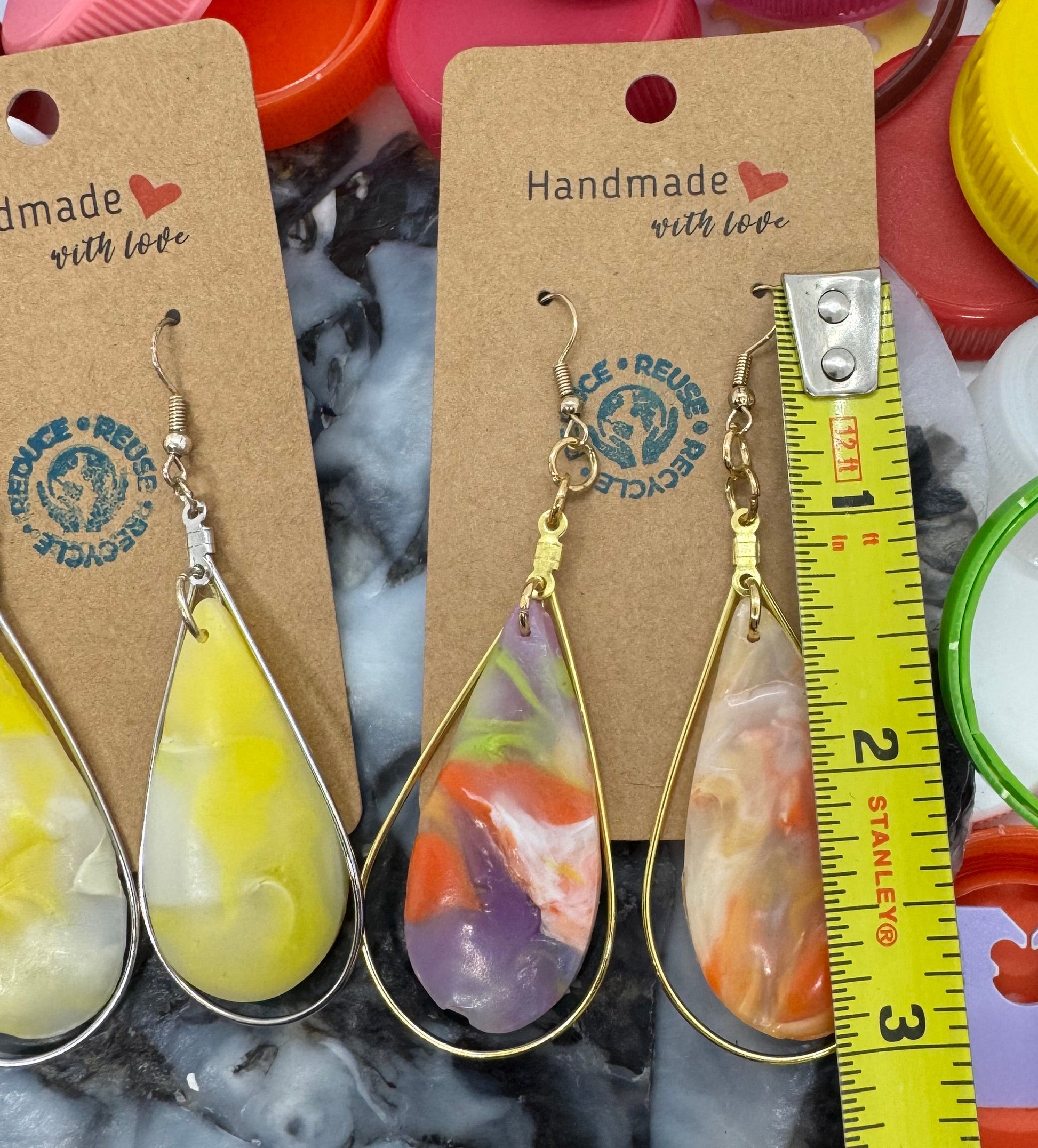 Colorful bottle caps with earrings and a measuring tape on a textured surface