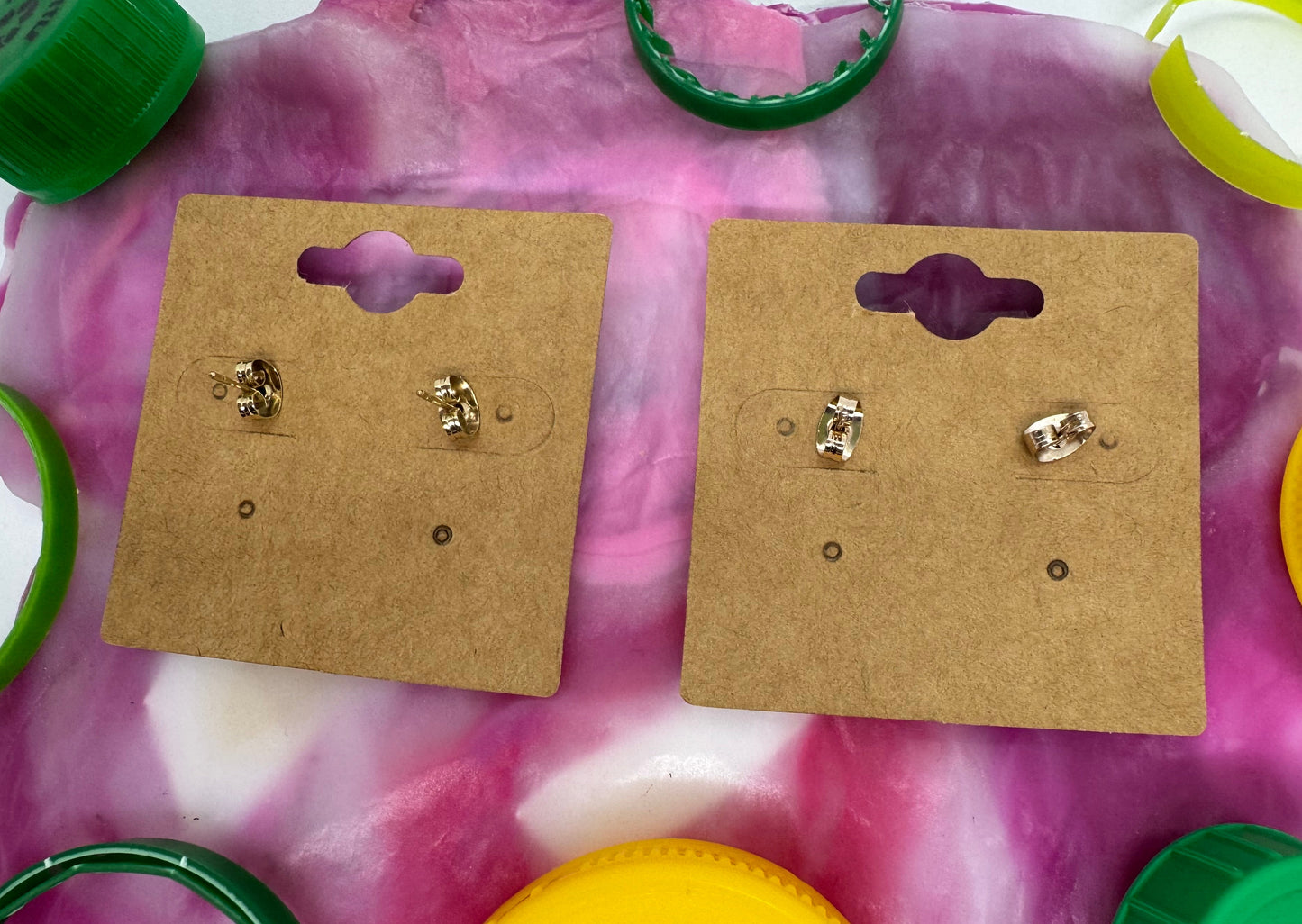 Gold earrings on brown card holders with colorful background