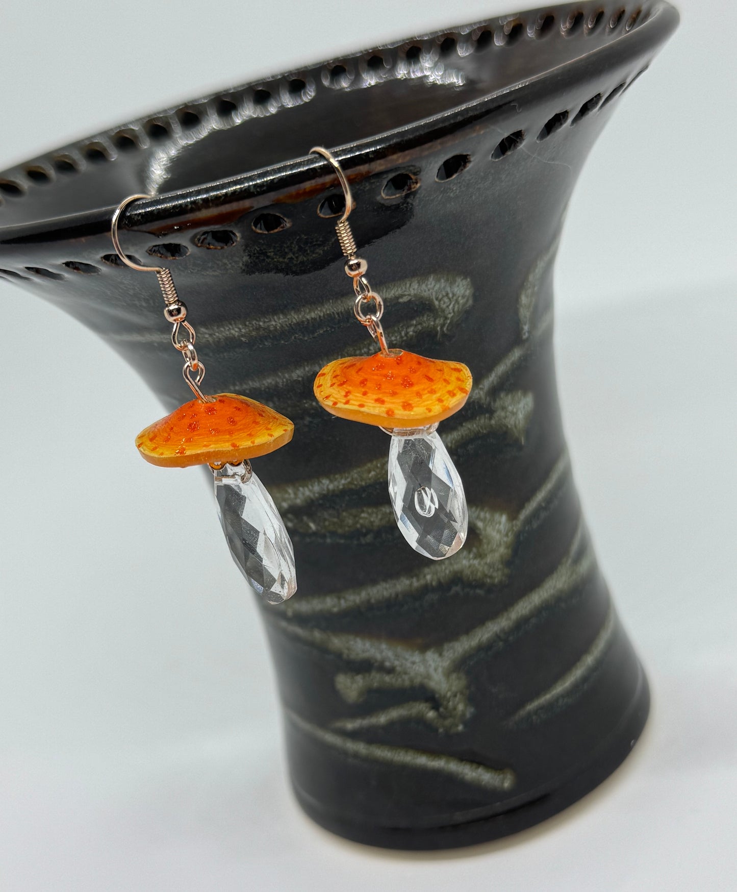 Pair of earrings with orange and clear stones on a black stand.