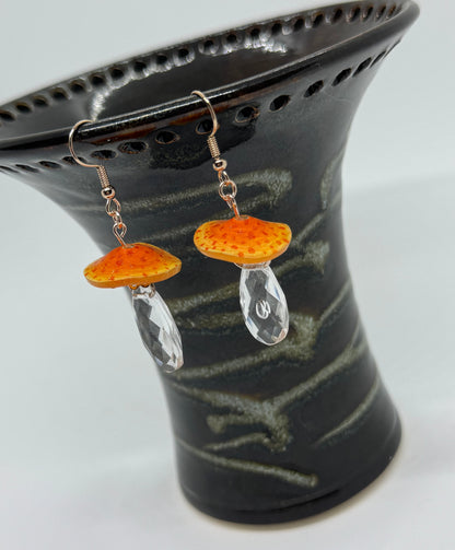 Pair of earrings with orange and clear stones on a black stand.