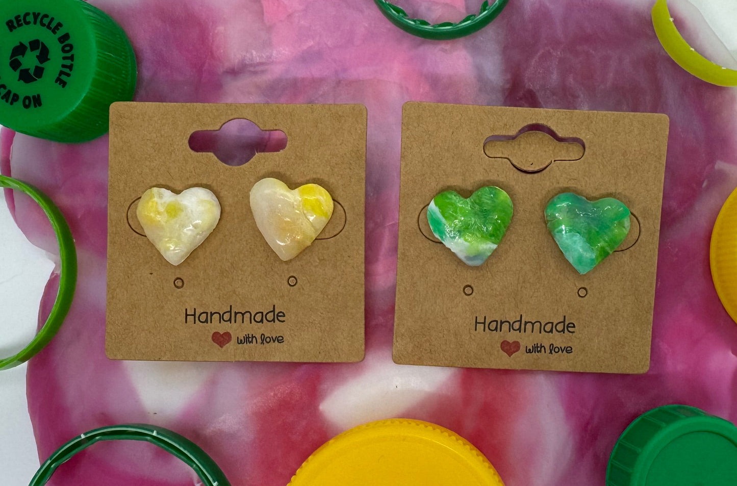 Heart-shaped earrings on display with colorful bottle caps and rings.
