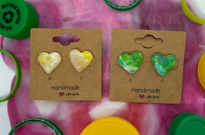 Heart-shaped earrings on display with colorful bottle caps and rings.