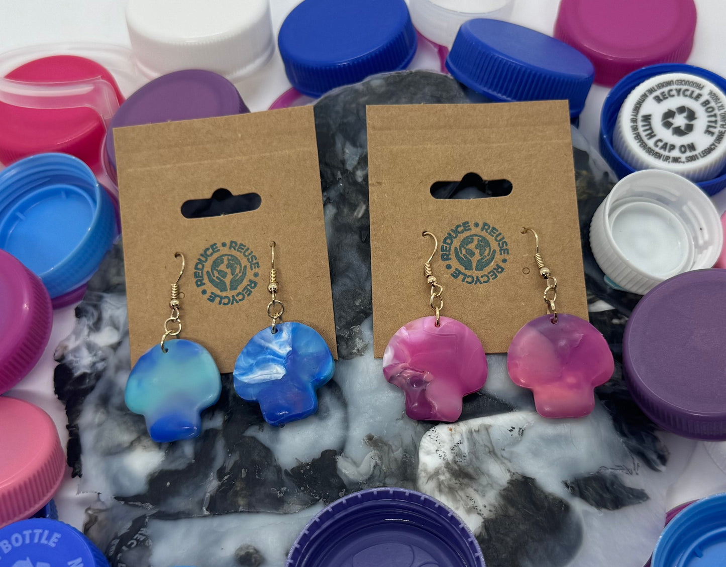 Colorful earrings on wooden cards surrounded by assorted bottle caps on a white background
