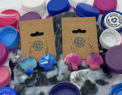 Colorful earrings on wooden cards surrounded by assorted bottle caps on a white background