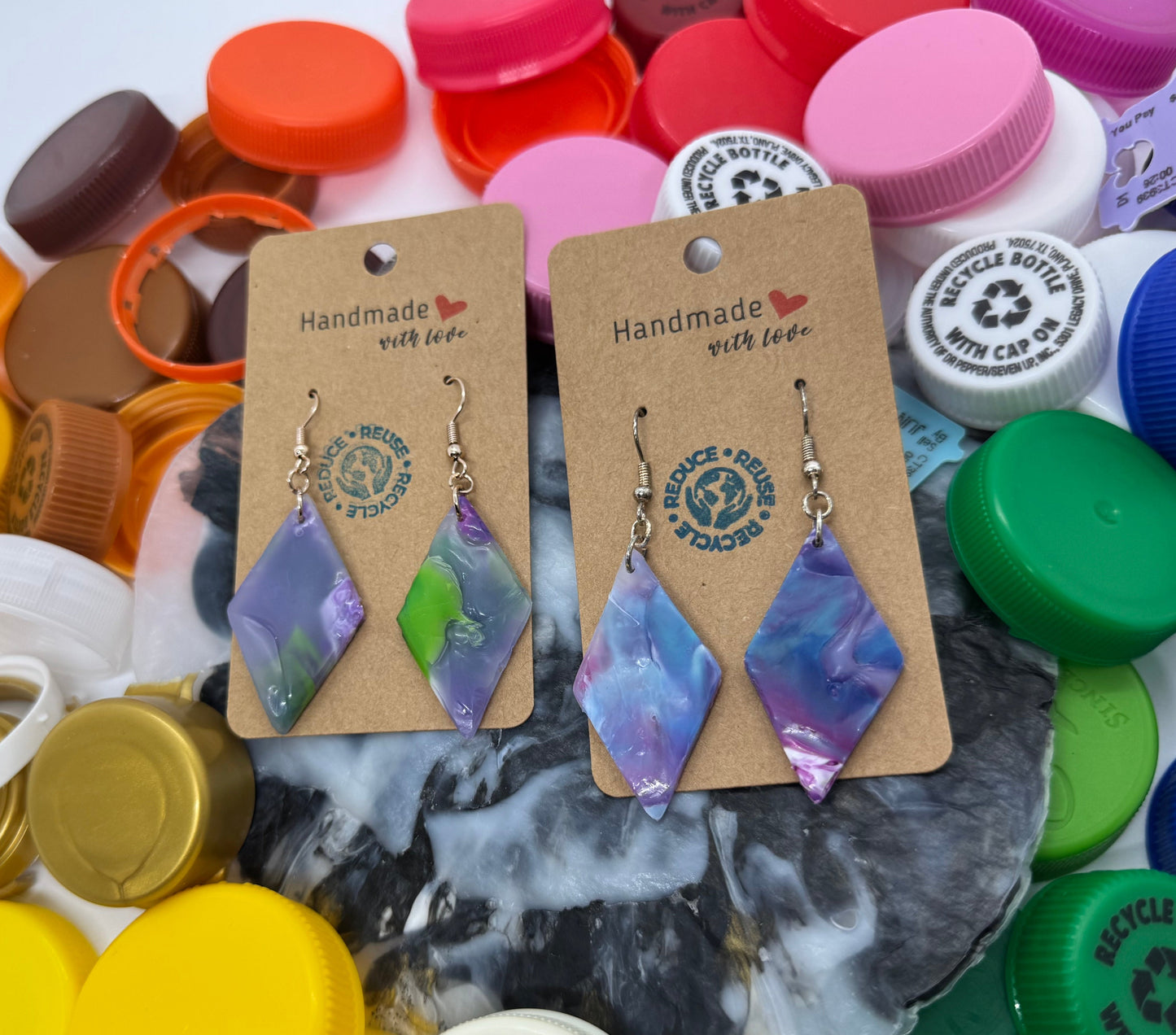 Pair of earrings on cards with 'Handmade with Love' text, surrounded by colorful bottle caps.