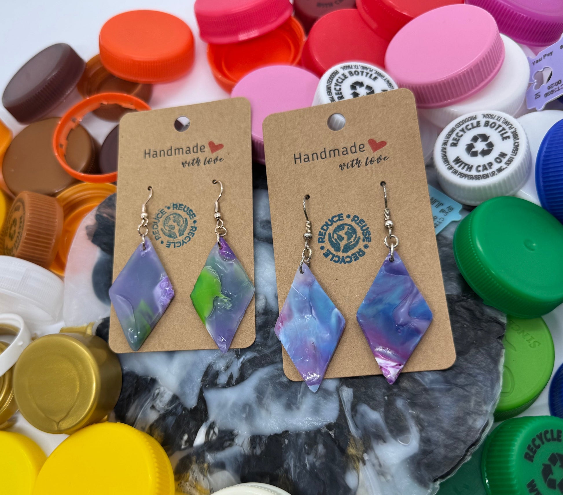 Pair of earrings on cards with 'Handmade with Love' text, surrounded by colorful bottle caps.
