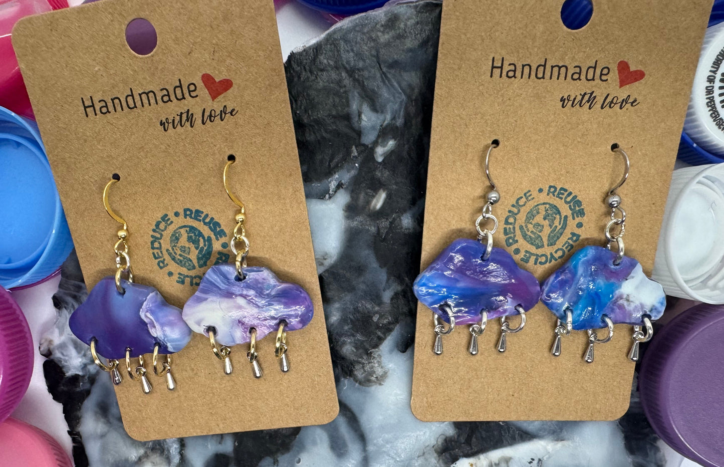 Pair of purple and blue earrings on brown card with 'Handmade with Love' text, surrounded by colorful bottle caps.