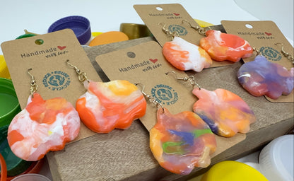 Colorful handmade earrings on display with various bottle caps in the background.