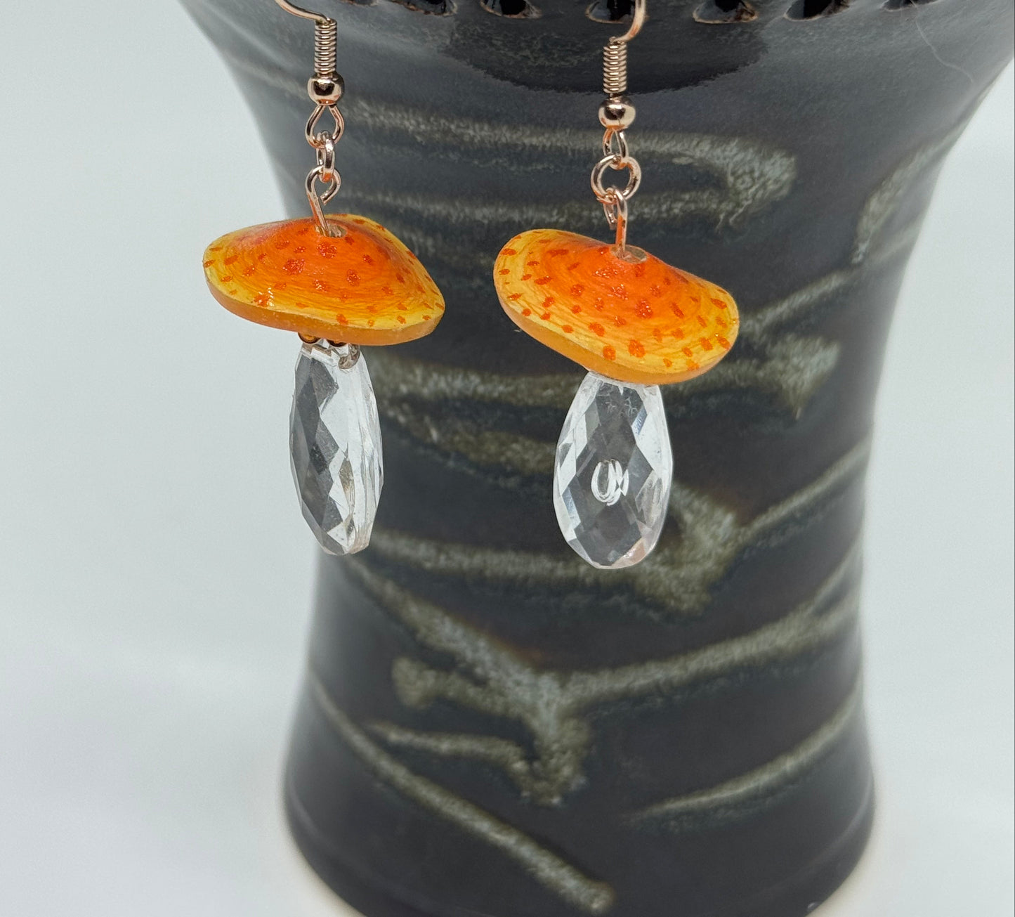 Pair of earrings with orange and clear stones on a dark textured background