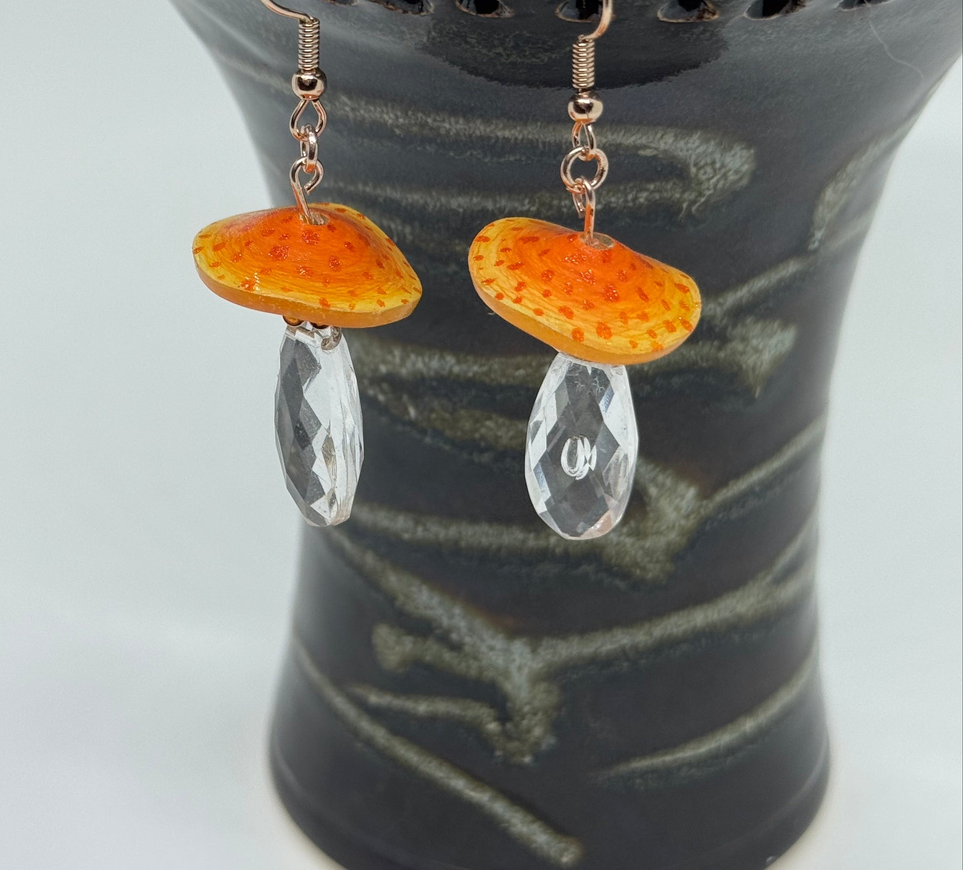 Pair of earrings with orange and clear stones on a dark textured background
