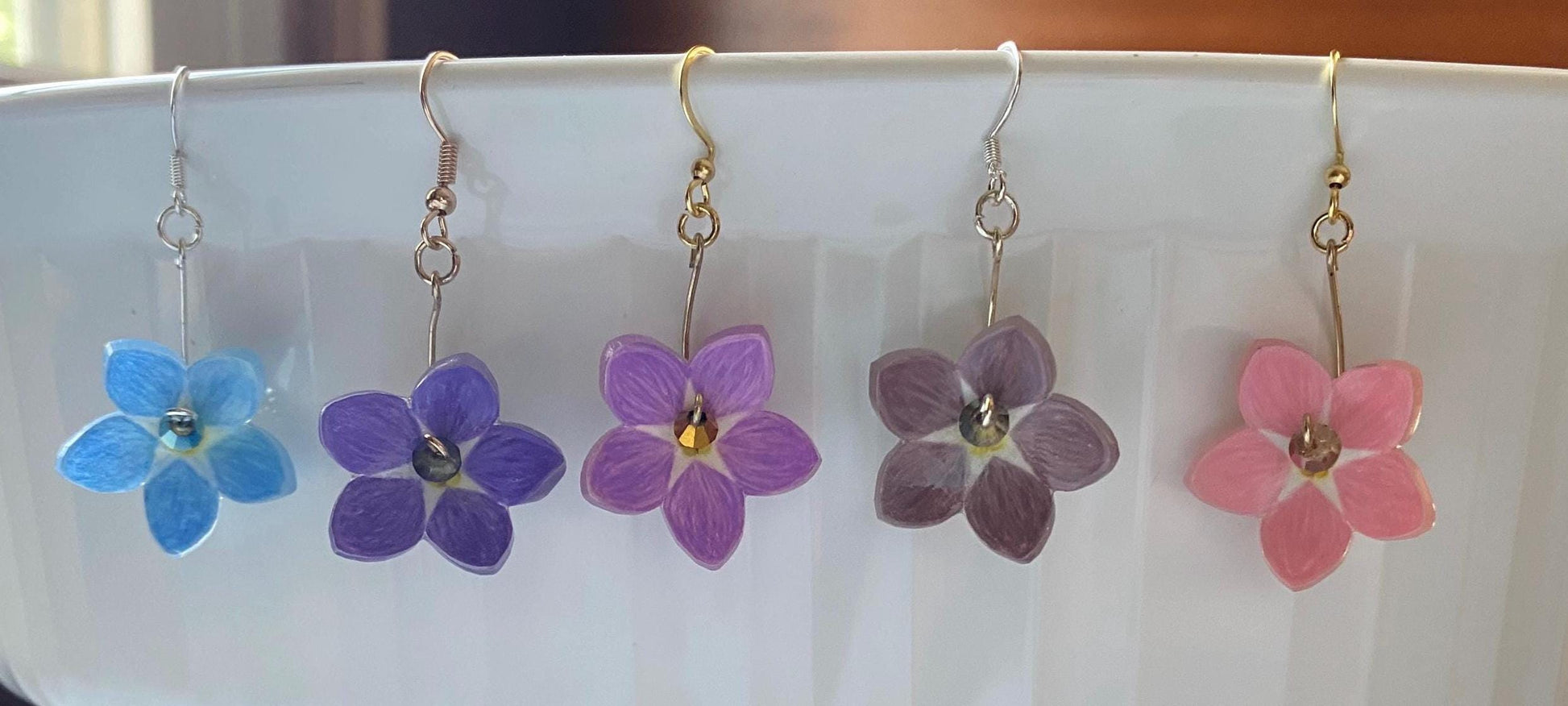 Set of five flower-shaped earrings in blue, purple, and pink on a white plate.