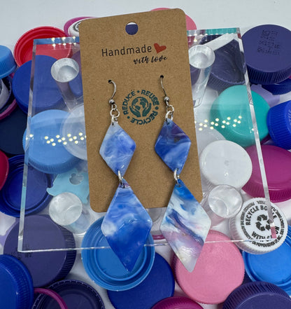 Colorful plastic bottle caps with a pair of blue and white earrings on a card, against a white background.