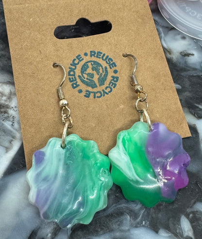 Colorful flower-shaped earrings on a cardboard card with recycling logo, surrounded by plastic bottle caps.