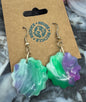 Colorful flower-shaped earrings on a cardboard card with recycling logo, surrounded by plastic bottle caps.