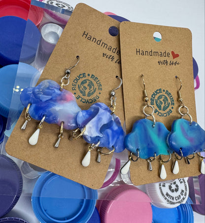Blue and white heart-shaped earrings on a cardboard display card with bottle caps in the background.