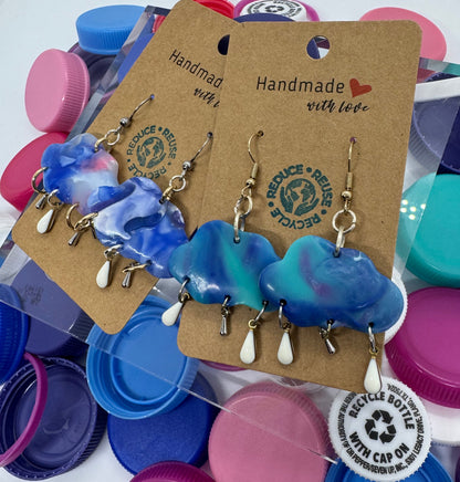 Blue and green earrings on a card with colorful bottle caps in the background