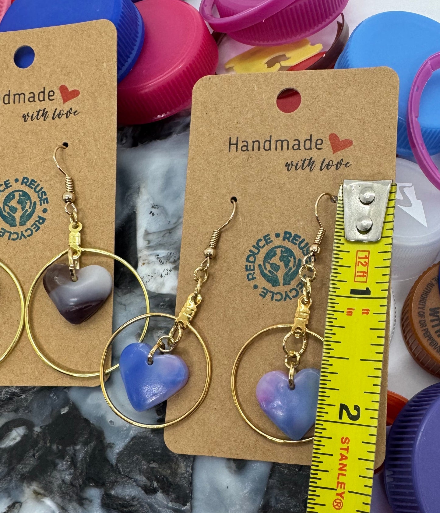 Gold hoop earrings with heart-shaped charms on a card, surrounded by colorful bottle caps.