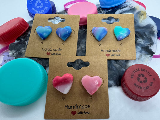 Heart-shaped earrings on a cardboard backing with 'Handmade' text, surrounded by plastic bottle caps.