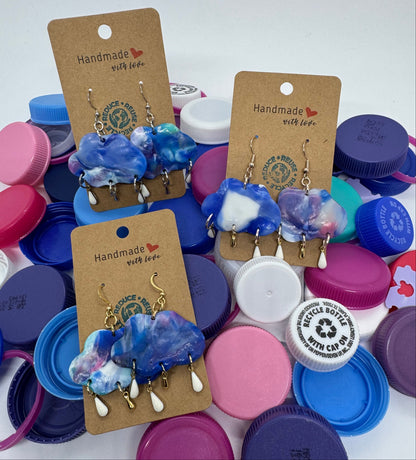 Pair of blue and white earrings on brown cards with colorful bottle caps in the background.