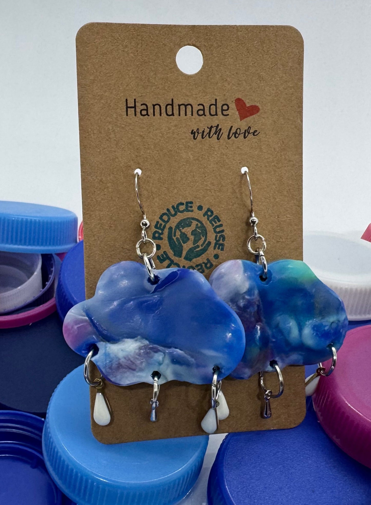 Blue and white patterned earrings on a cardboard backing with colorful bottle caps in the background.