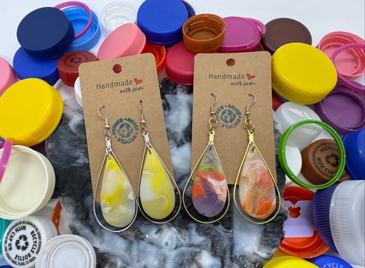 Pair of teardrop-shaped earrings on brown cards with 'Handmade with Love' text, surrounded by colorful bottle caps.