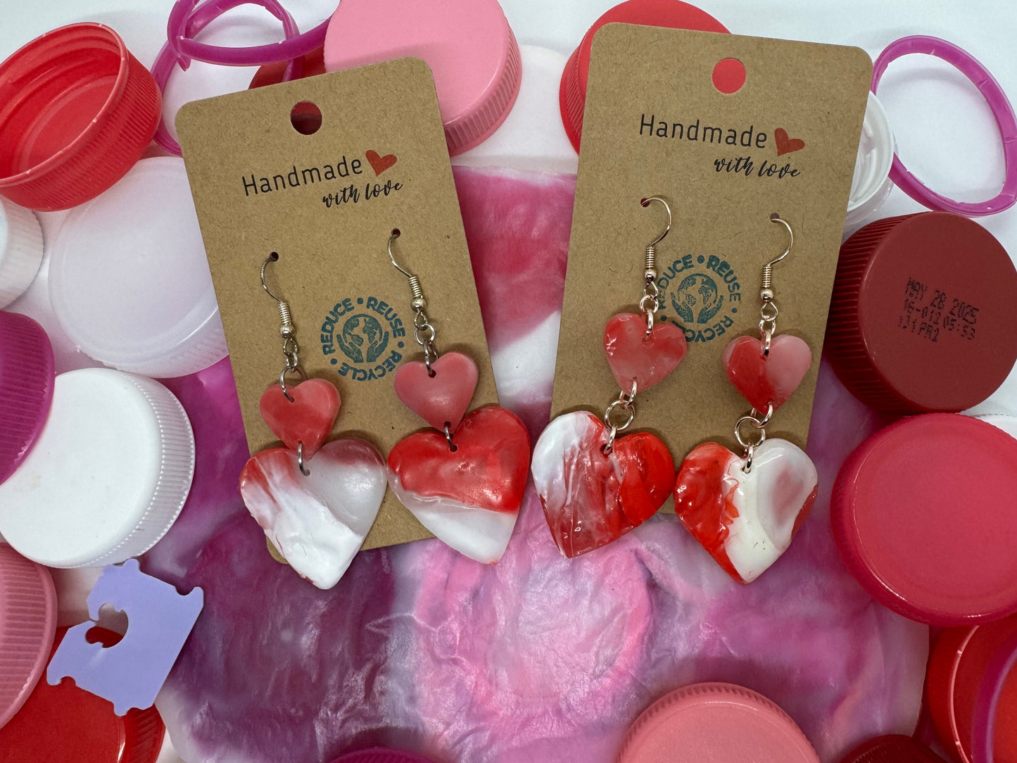 Heart-shaped earrings on brown cards with colorful bottle caps in the background