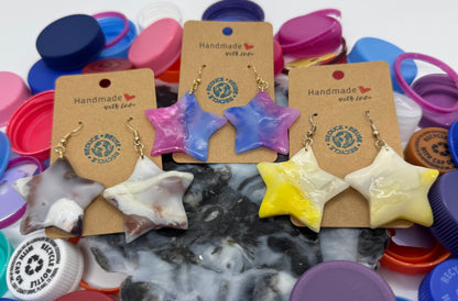 Star-shaped earrings on display with colorful bottle caps in the background