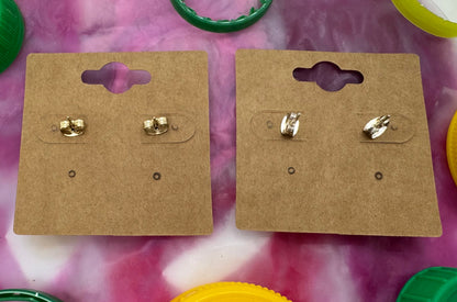 Gold earrings on cardboard cards with colorful bottle caps on a pink and white background